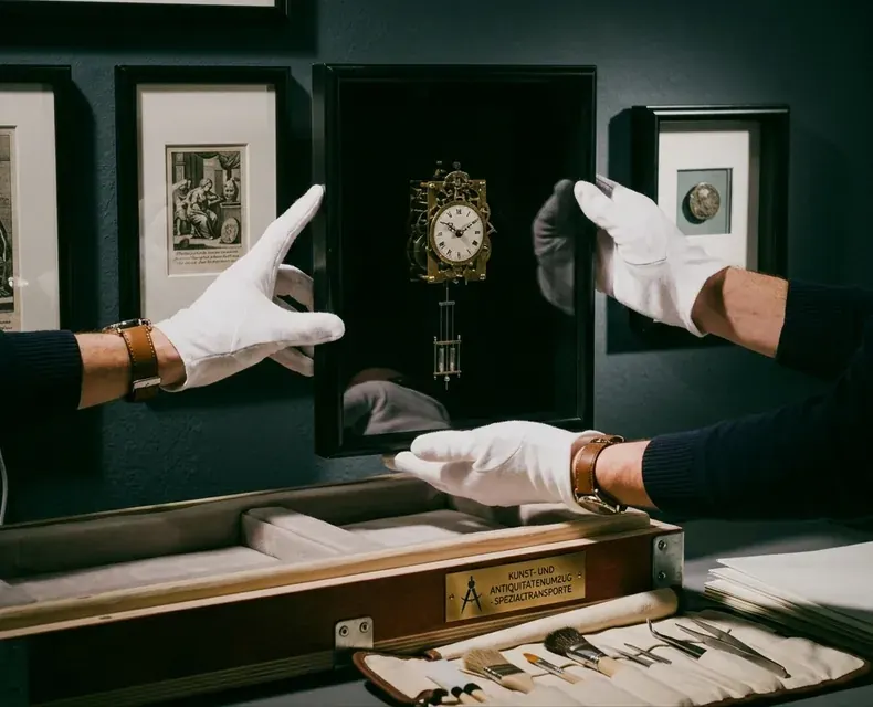 Behandschuhte Hände sichern eine antike Uhr für den Kunst- und Antiquitätentransport ab Düsseldorf